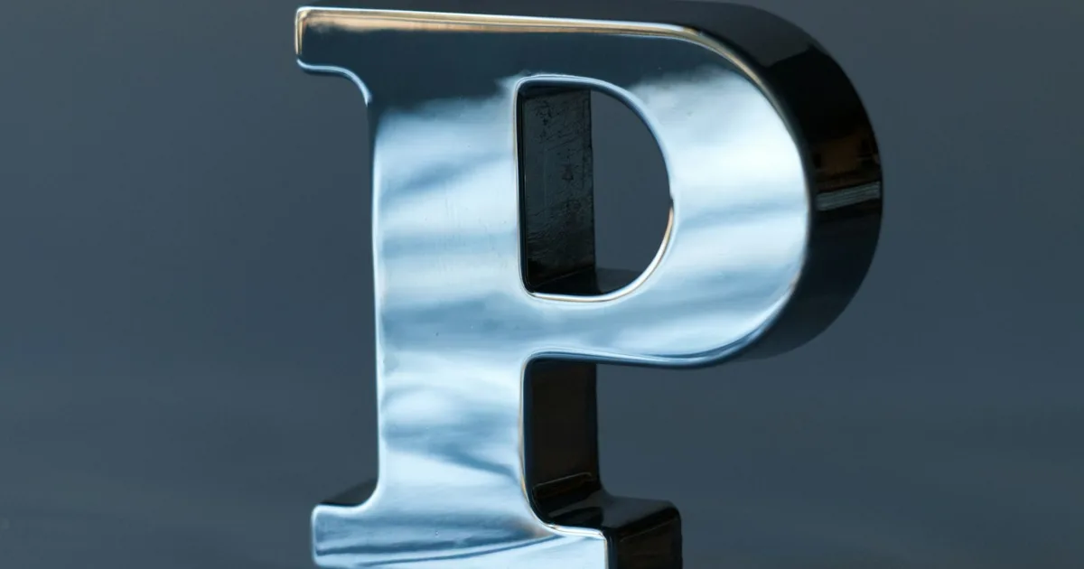 Mirror-polished metal dimensional letter P on a dark wall – example of metal signage lettering